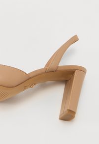 Beige sandaalit, joissa on neliön muotoinen paljas korko, avoin varvas ja minimalistiset remmit. Tasainen pinta, jossa on hienovaraisia ompeluyksityiskohtia.