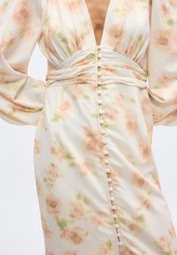 Dress with soft peach and green floral print, deep V-neck, ruched waist, long puffed sleeves, and a vertical row of fabric-covered buttons.