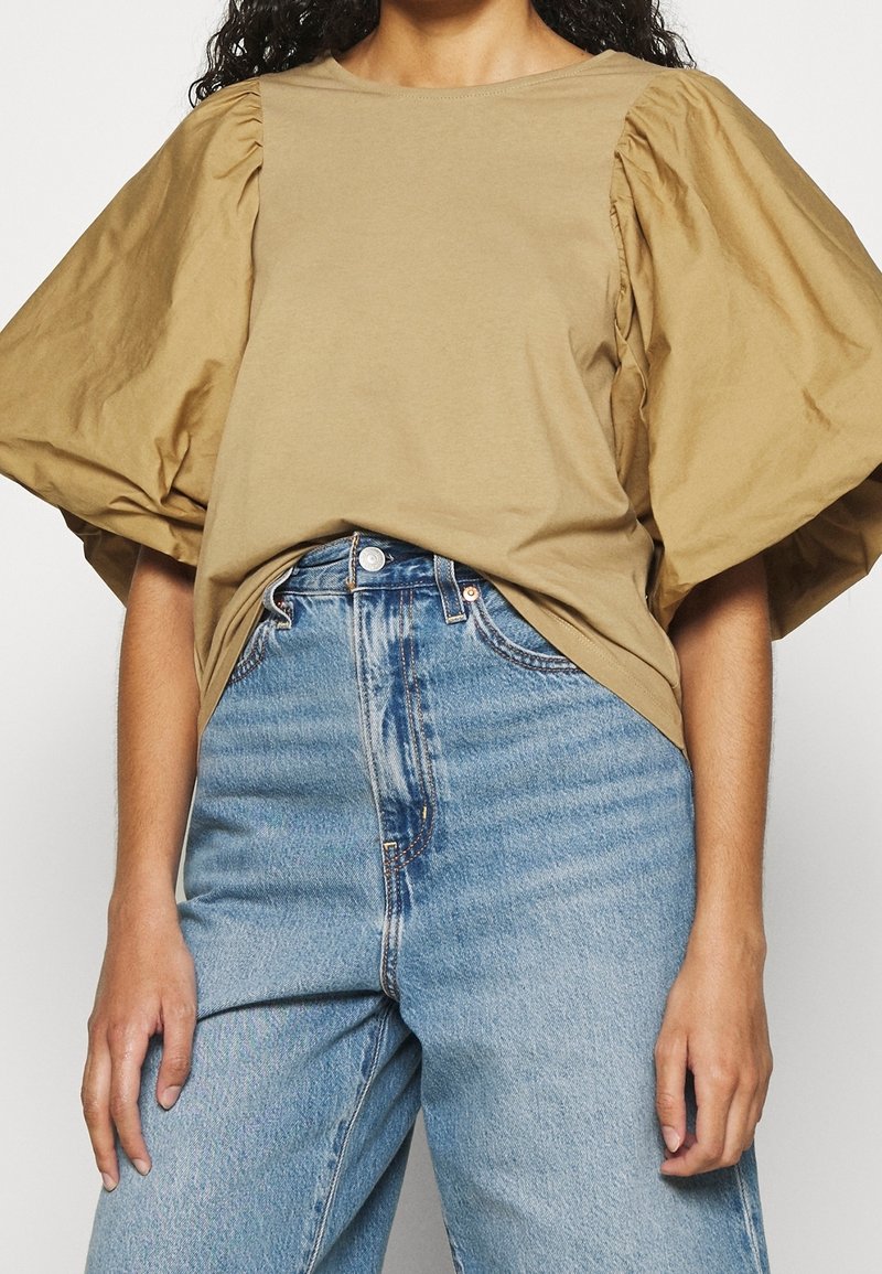 Krátký rukáv béžový top s objemnými balónovými rukávy, vyrobený z měkké bavlny. V kombinaci s modrými džíny s vysokým pasem.