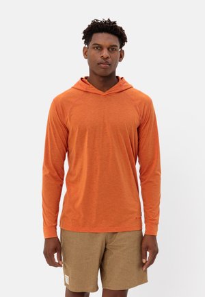 Langdurige mouwen, oranje hoodie met een ontspannen pasvorm en raglanmouwen, gecombineerd met tan shorts. De stof lijkt lichtgewicht en gestructureerd.