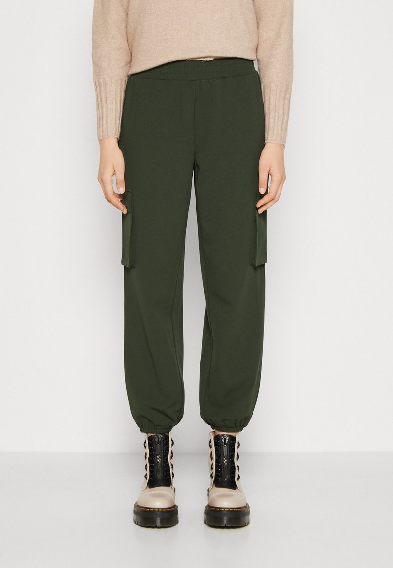 Pull beige à poignets côtelés associé à un pantalon cargo jogger vert olive et des bottines beiges claires à lacets avec semelles noires.