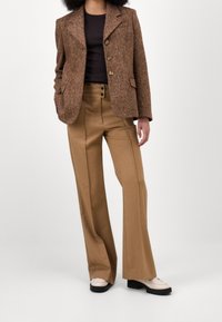 Brun hounds-tooth blazer med notched lapels och tre knappar, kombinerad med högmidjade beiga byxor och krämfärgade platåskor.