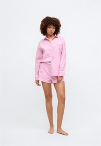 Ροζ ριγέ κοντομάνικο πουκάμισο με μία τσέπη και ταιριαστά σορτς με αντίθετη μέση. Απαλή ύφανση και άνετη εφαρμογή.