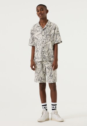 Korte mouwen overhemd met knopen en bijpassende shorts in wit met zwart bladpatroon. Gecombineerd met witte sneakers en gestreepte sokken.