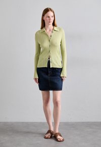 Light green ribbed cardigan with a collar and button closure, paired with a dark denim skirt. Brown strappy sandals complete the outfit.