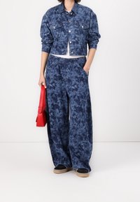 Kurtka dżinsowa i szerokie spodnie w ciemnoniebieskim kolorze z kwiatowym wzorem. Posiadają elastyczną talię i kieszenie. Trzyma czerwoną torebkę.