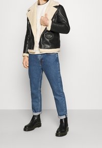 Czarna skórzana kurtka z beżowym futerkiem z ekologicznego włosia przy kołnierzu, z zamkiem z przodu, dwie kieszenie, zestawiona z niebieskimi dżinsami i czarnymi botkami za kostkę.