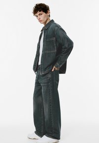 Donkerdenimjack met een zak, gecombineerd met brede donkerdenimbroeken. Een wit t-shirt eronder en witte sneakers complementeren de outfit.
