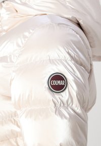 Veste matelassée rembourrée en matériau rose clair brillant avec un design matelassé, comportant un patch circulaire du logo Colmar sur la manche.