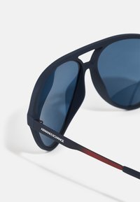 Ochelari de soare rotunjiți, de culoare bleumarin, cu lentile gradient în nuanțe de albastru. Rame cu finisaj mat, având logo-ul argintiu "AR MAN EXCHANGE" pe tâmplă și accente roșii pe braț.