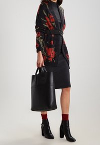 Stickad kofta med blommönster i mörka nyanser, bälte i midjan; ribbad klänning, svart tote-väska och klackade ankelstövlar fulländar looken.