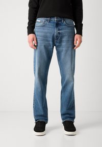 Lyseblå denimjeans med rett benkutt, metallknapplukking og frontlommer. Bært med svarte joggesko, som gir et avslappet utseende.