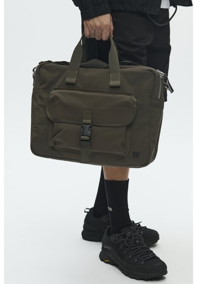 Sac en nylon vert olive avec deux poignées supérieures, poche à rabat avant sécurisée par une boucle, fermeture éclair et détail de marque sur le côté.