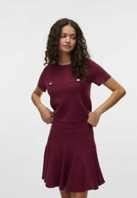Burgundský dvoudílný set obsahující upnutý top s krátkým rukávem a dvojicí kapes a rozšířenou sukni s sklady na lemu.