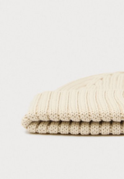 Folded cream-colored knitted beanie with a ribbed texture, featuring a soft, thick material and a subtle, even pattern throughout.