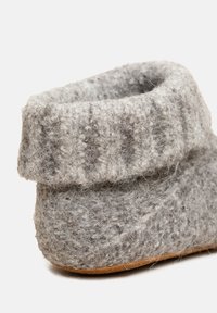 Szare filcowe kapcie z zagiętym mankietem i fakturowaną powierzchnią. Wykonane z miękkiego materiału przypominającego wełnę, z brązową skórzaną podeszwą.