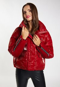 Giacca imbottita rossa con finitura lucida, colletto alto e tasche con zip; presenta una vestibilità rilassata e dettagli di cucitura in evidenza.