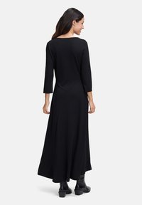 Zwarte maxi-jurk met lange mouwen en een ronde halslijn, met een vloeiende silhouet. Heeft diagonale naaddetails en wordt gedragen met zwarte enkellaarsjes.