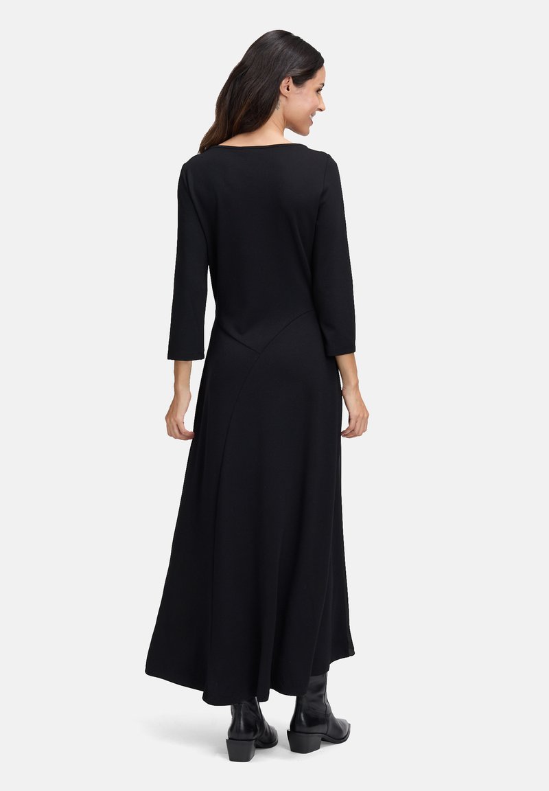 Zwarte maxi-jurk met lange mouwen en een ronde halslijn, met een vloeiende silhouet. Heeft diagonale naaddetails en wordt gedragen met zwarte enkellaarsjes.