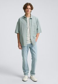 Lichtgroen short-sleeve shirt met een zak, gecombineerd met lichtblauwe jeans en witte sneakers. Gelaagd materiaal en een relaxte pasvorm.