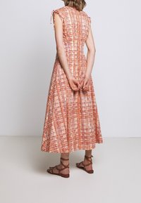 Maxi mekko, jossa on teksturoitu oranssi ja kerma-valkoinen ruudukko. Ominaisuuksina hihattomat hihat ja solmimisnauhat olkapäillä. Yhdistetty ruskeisiin remmisandaaleihin.