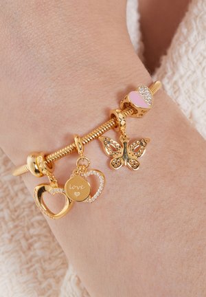 Gouden charmarmband met hart- en vlindermotieven, met roze en heldere accenten, om een pols met zichtbare textuur.
