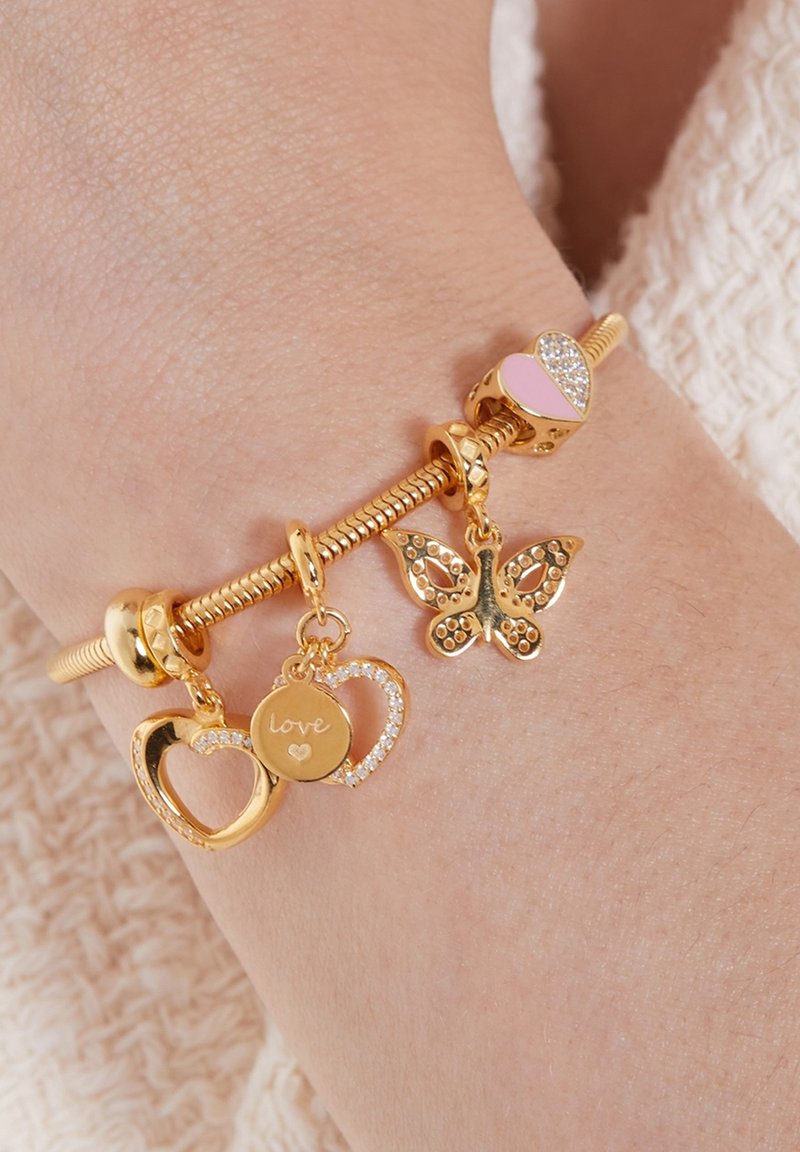 Gouden charmarmband met hart- en vlindermotieven, met roze en heldere accenten, om een pols met zichtbare textuur.