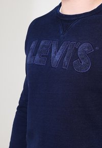Sudadera azul marino hecha de una mezcla de algodón, presenta un logo grande y texturizado de Levi's en relieve en la parte frontal y un cuello redondo.