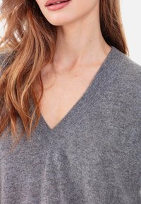 Pull gris à col en V en matière douce, présentant un tricot texturé et une coupe décontractée. Vue en gros plan mettant en avant le col et les détails du tissu.