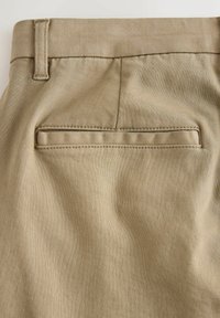 Khaki trousers featuring a smooth texture, a single back pocket, and a belt loop. The fabric exhibits a subtle twill pattern.