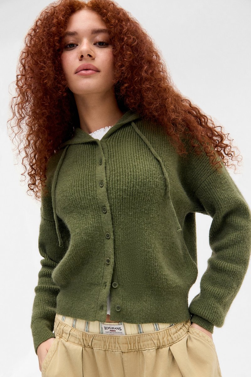 Cárdigan verde de punto con capucha, textura acanalada, cierre de botones y cordones, combinado con pantalones beige de cintura elástica con rayas.