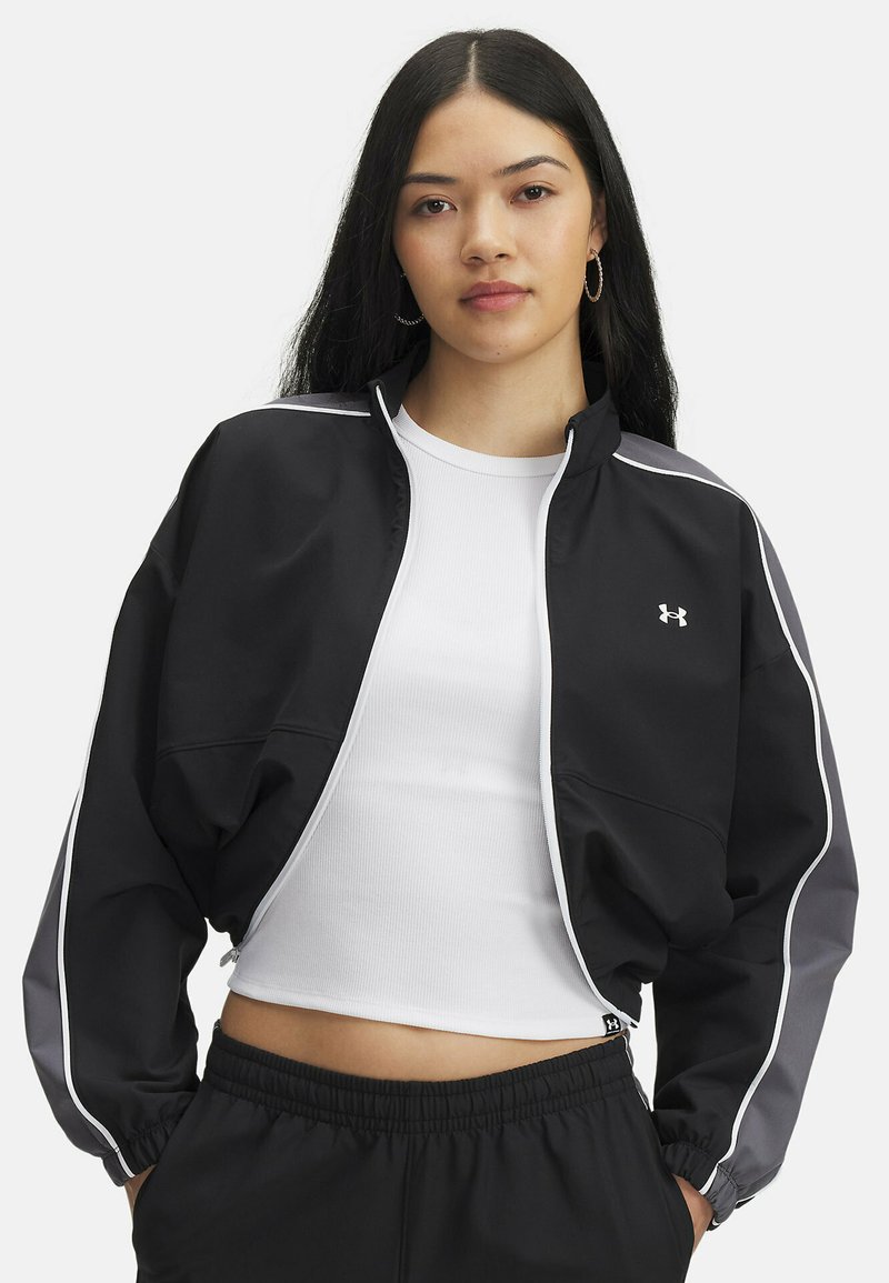 Veste de sport noire avec des accents gris, poignets élastiques et fermeture éclair à l'avant. Présente des liserés blancs et un logo Under Armour sur la poitrine.