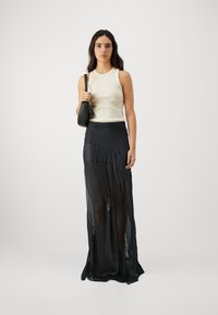 Jupe maxi noire avec un design en superposition transparente et des accents texturés. Associée à un haut sans manches crème ajusté et un petit sac noir.