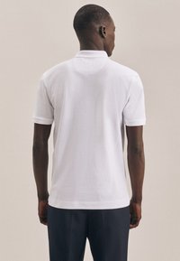 Polo shirt bianco con maniche corte, caratterizzato da un colletto classico, una texture morbida e un orlo diritto. Design leggermente aderente.