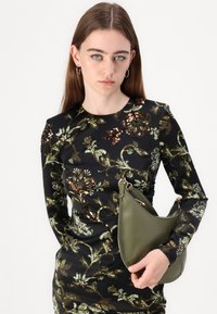 Juoda suknelė su žydinčių sequin raštu žaliai ir auksinėmis spalvomis; modelis laiko išlenktą alyvų žalią rankinę su metaliniu dirželiu.