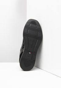 Semelle de sneaker noire avec caoutchouc texturé, présentant des rainures horizontales et verticales pour une meilleure adhérence. Logo et 'Fabriqué en Italie' embossés.