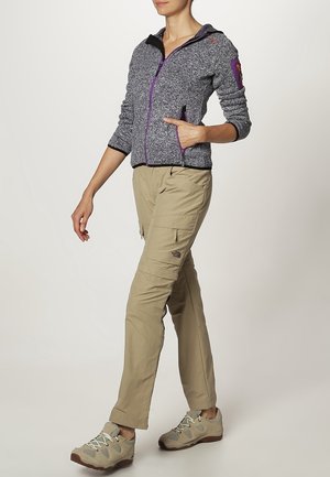 Grijze fleecejack met paarse ritsdetails, beige cargobroek met zijzakken en lichtgekleurde wandelschoenen met gripzolen.