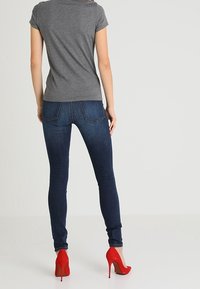 Grå t-shirt med kort ärm som matchas med mörkblå tajta jeans och röda högklackade skor; slät tygtextur och figurnära design.