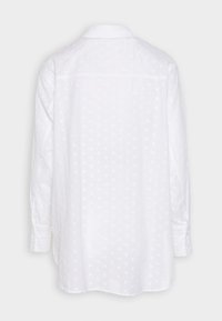 Camicia bianca a maniche lunghe con un motivo a pois testurizzati. Presenta un colletto e polsini con bottoni, con una vestibilità ampia e rilassata.