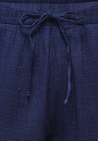 Primo piano di pantaloni blu scuro con vita elastica e coulisse annodata sul davanti.