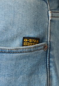 Poche de jean en denim bleu clair avec une petite étiquette de la marque G-Star Original noire et jaune cousue sur le bord supérieur de la poche.