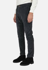 Pantaloni in velluto a coste di un grigio scuro con una vestibilità affusolata, dotati di chiusura a bottone, cordoncino e orli arrotolati, abbinati a stivali in suede neri.