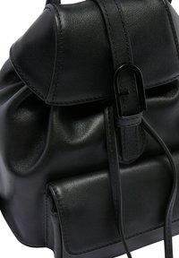 Zaino in pelle nera con una texture morbida, forma arrotondata, chiusura a pattina e una bretella prominente. Presenta cuciture decorative e una tasca piccola.