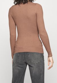 Haut marron côtelé à manches longues avec une silhouette ajustée, doté d'un col rond et d'un motif en maille texturée. Associé à un jean gris foncé.