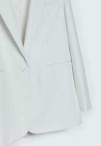 Blazer blanc à un bouton avec col cranté et deux poches avant horizontales, présenté sur un fond clair.