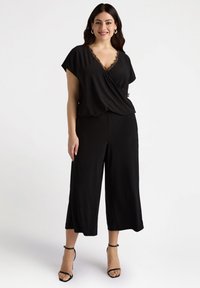 Czarny zestaw składający się z bluzki z krótkim rękawem z koronkowym wykończeniem i spodni z szeroką nogawką. Gładki, lekki materiał o luźnym kroju.