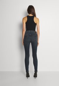 Svart linne i kombination med mörkblå skinny jeans. Jeanserna har en design med fem fickor och en lätt blekning vid låren.