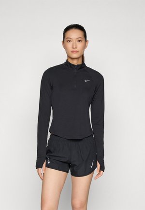 Svart atletisk zip-up topp med lange ermer, kombinert med svarte shorts. Begge har Nike-logoen. Glatt stoff, tettsittende design.