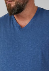 Niebieska koszulka V-neck wykonana z miękkiego, lekkiego materiału o subtelnej teksturze, z krótkimi rękawami i luźnym krojem.