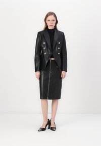Svart lær dobbeltradet blazer med metallknapper, kombinert med et svart lær blyantskjørt med glidelås foran. Høyhælte sko.